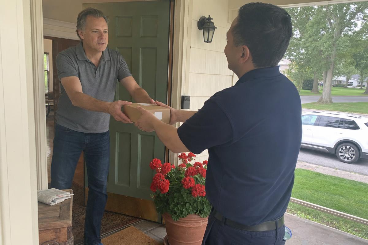 A man receiving a discreet REX MD telehealth shipping box at his front door from a delivery driver