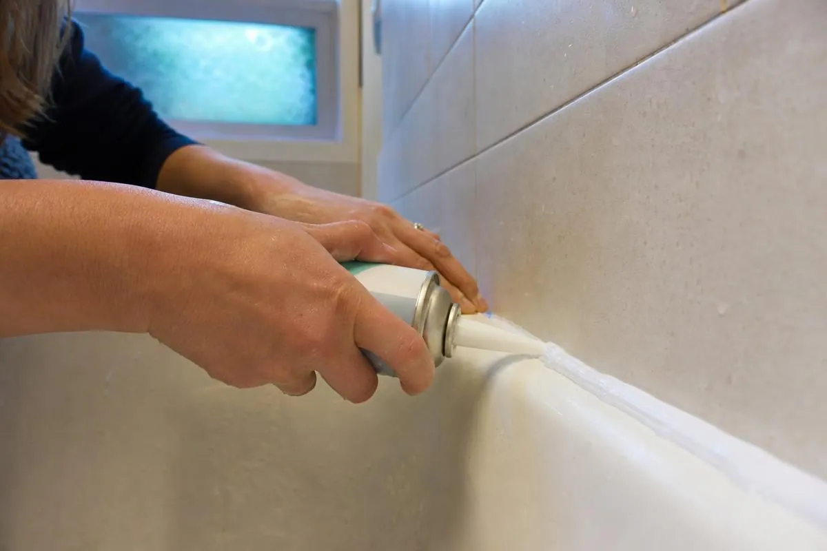 Close-up of hands applying Flex Shot rubber sealant along a bathtub seam