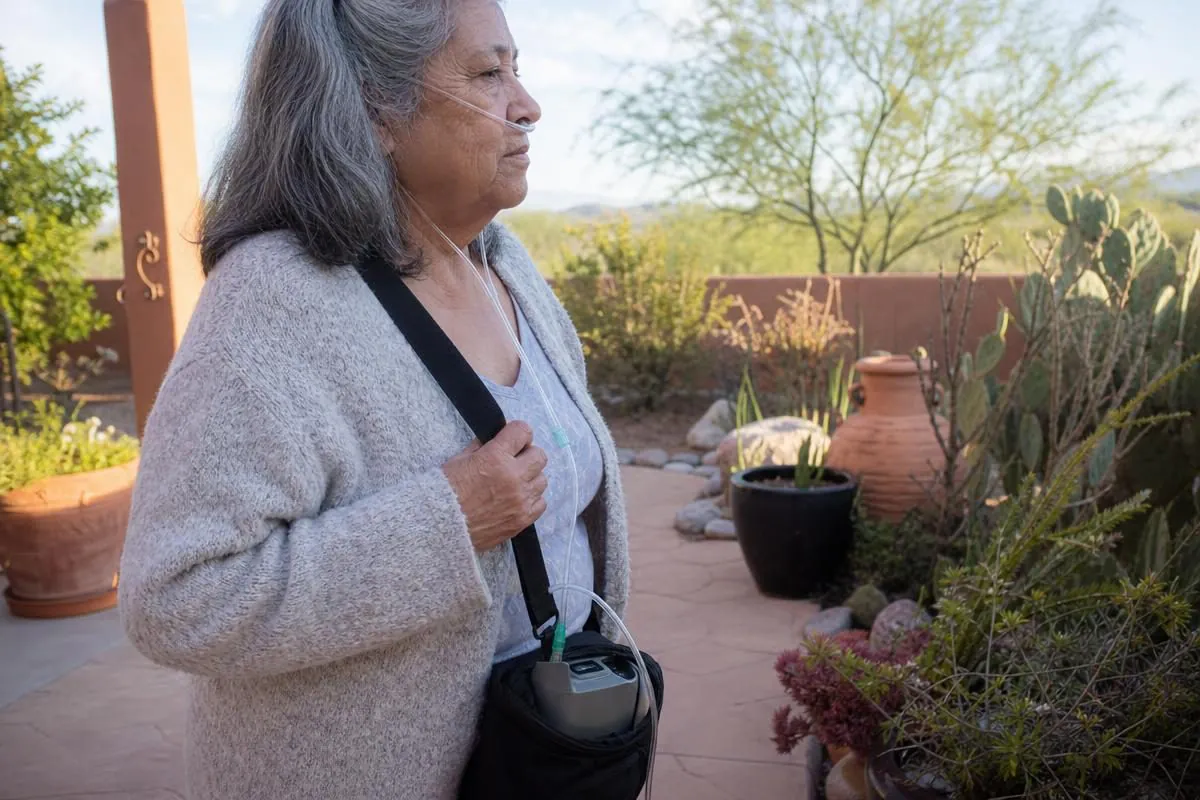 An older woman walking outdoors using an Inogen One portable oxygen concentrator