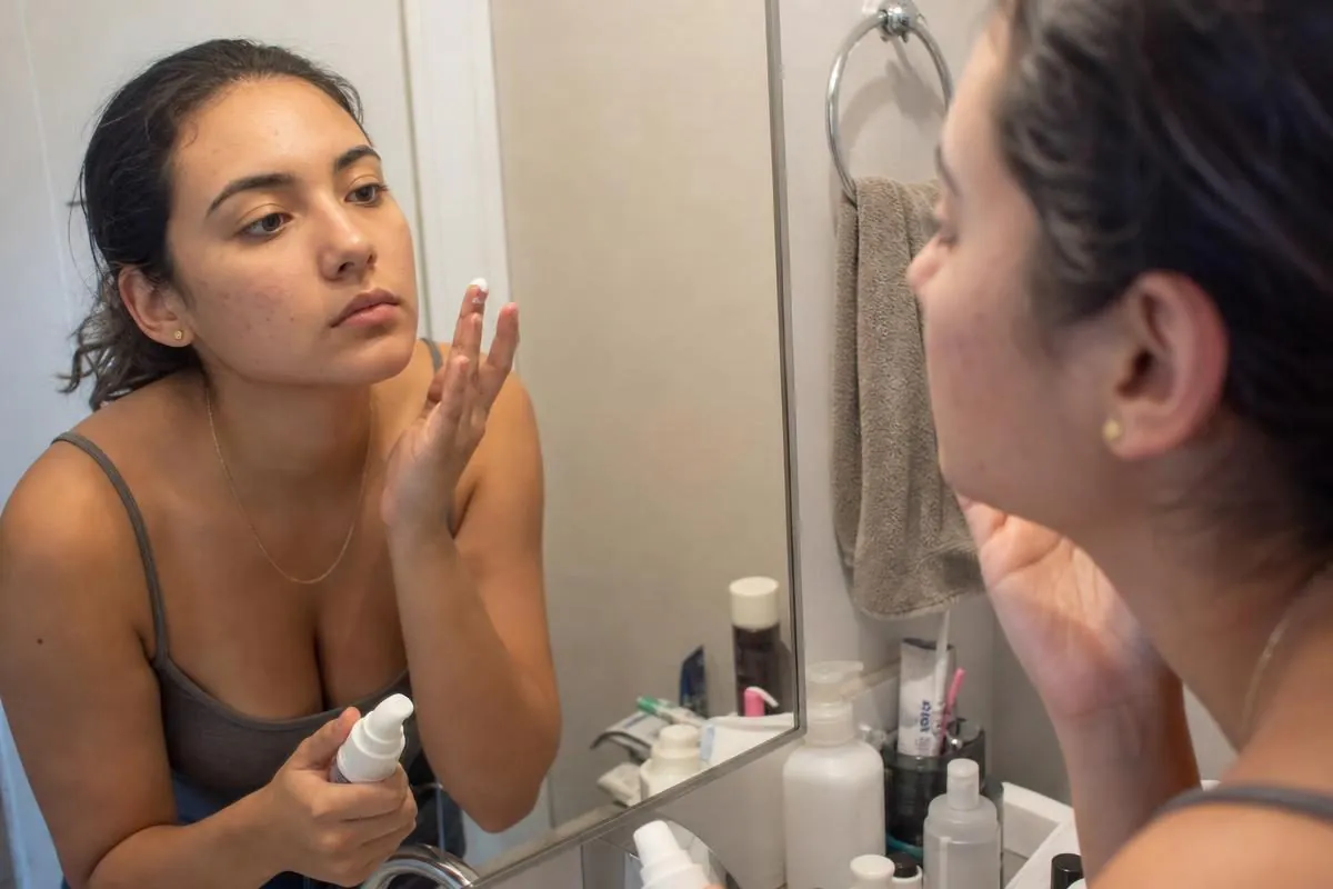 A young woman applying Proactiv Solution acne treatment at the bathroom mirror