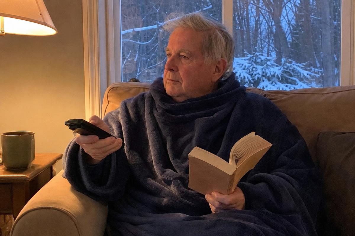 An older man relaxing on the couch wearing a Snuggie blanket with sleeves