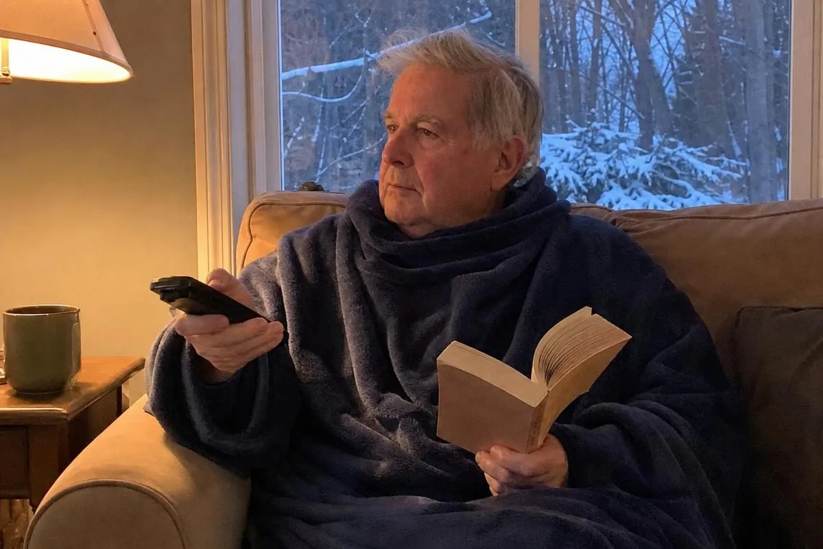 An older man relaxing on the couch wearing a Snuggie blanket with sleeves