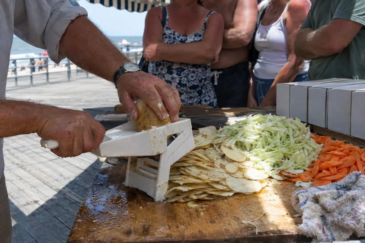 A boardwalk pitchman's hands slicing potatoes through a vegetable slicer while a crowd watches the demonstration