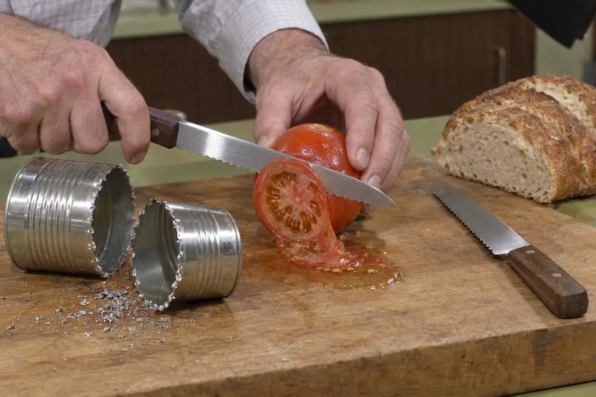 A serrated knife slicing a tomato beside a sawn tin can, the demo from one of the best infomercials of all time